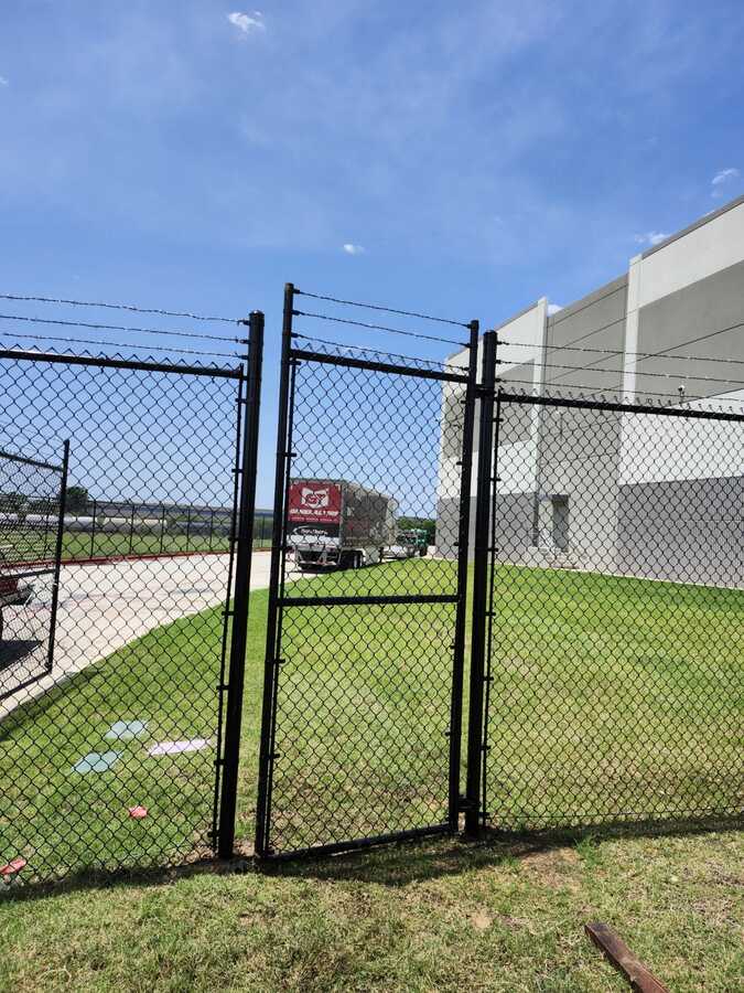 Black chain link fence and walk gate with barbed wire at a commercial property