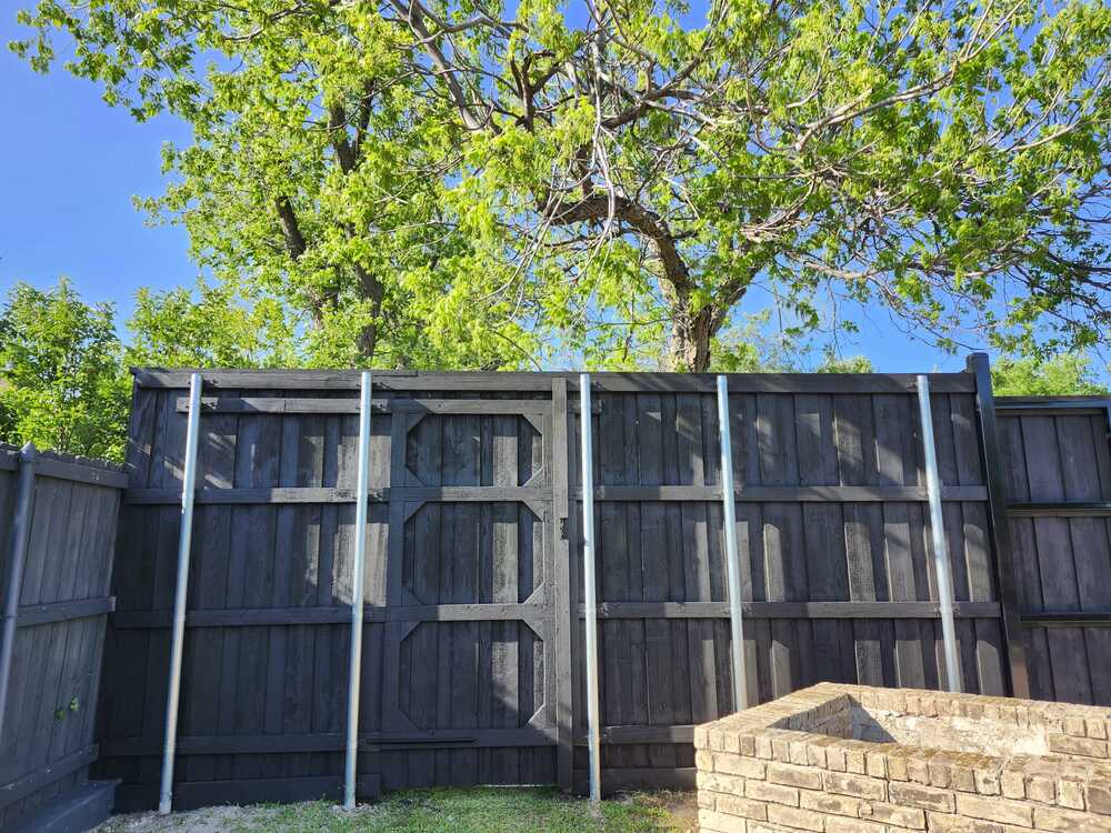 Black-stained wood fence with cross-braced gate and galvanized steel posts