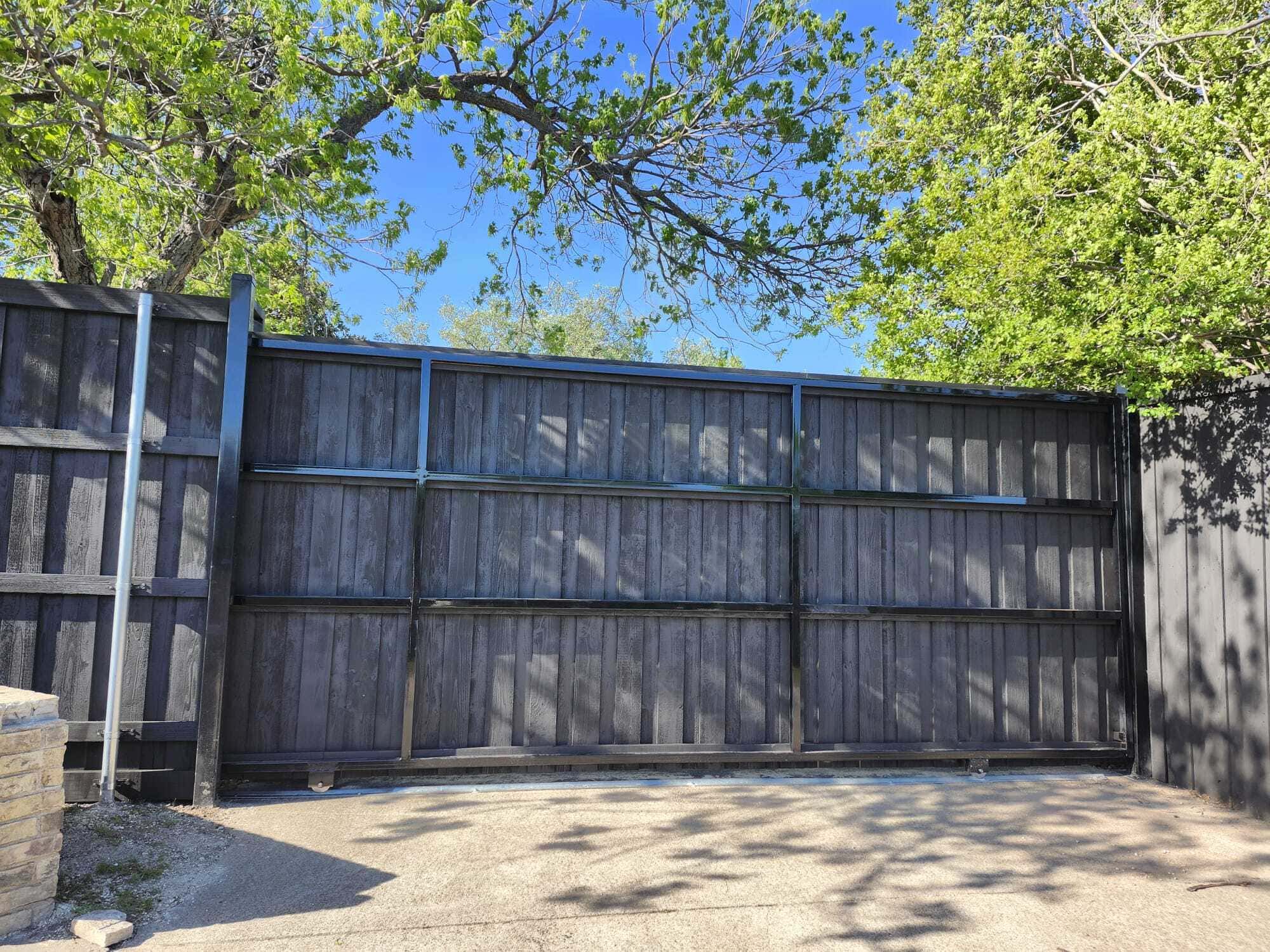 Black-stained wood sliding driveway gate with steel frame across a concrete drive