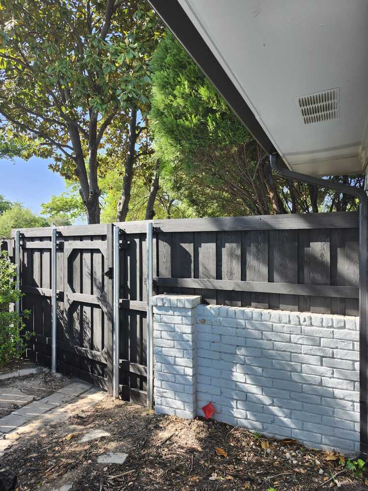 Black wood fence and walk gate with steel posts along a painted brick wall