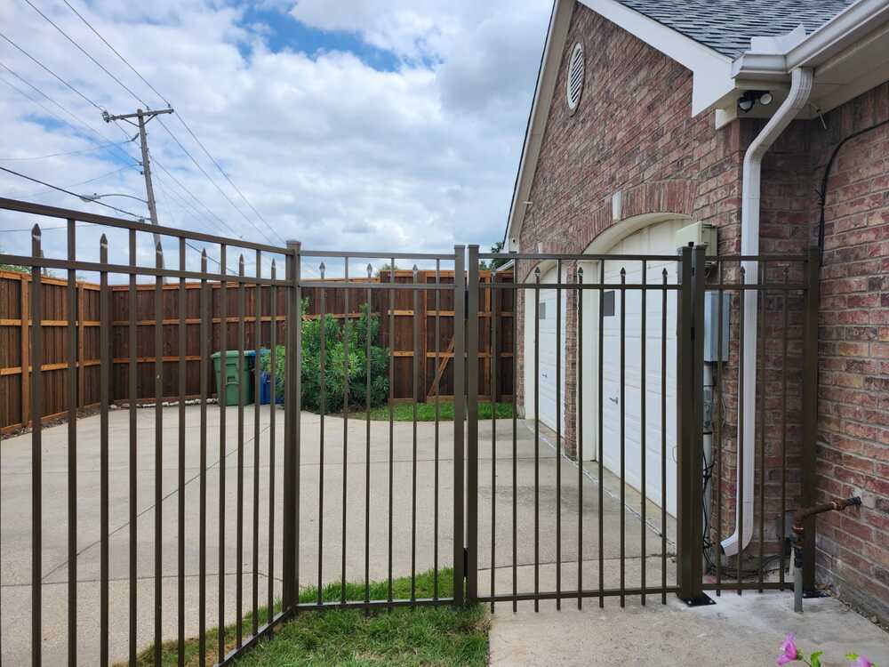 Bronze aluminum picket fence and walk gate with spear-top finials beside a garage