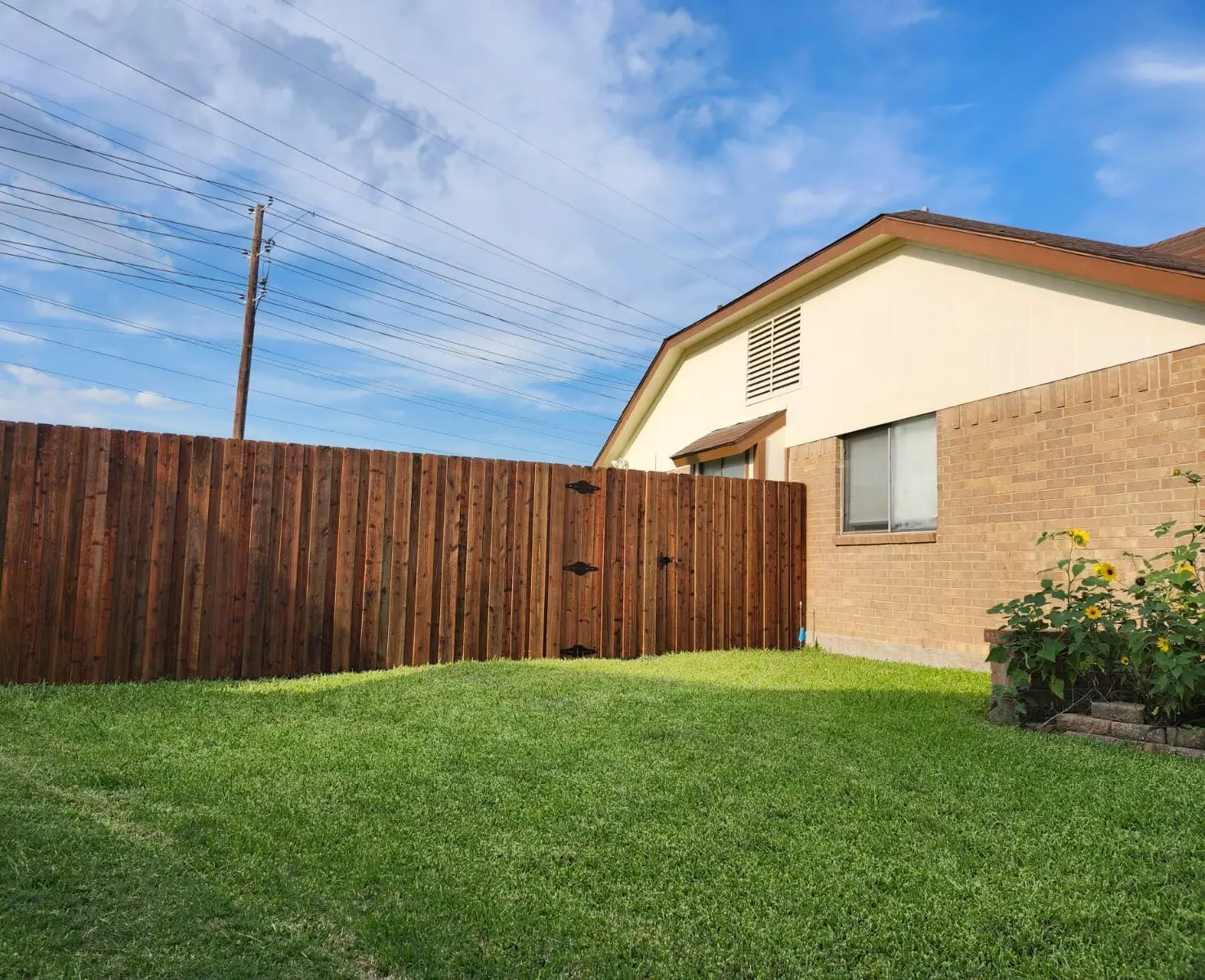 Stained cedar privacy fence with a matching walk gate beside a brick home