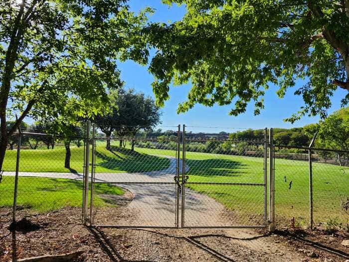 Galvanized chain link fence with double swing gates at a grassy field entrance