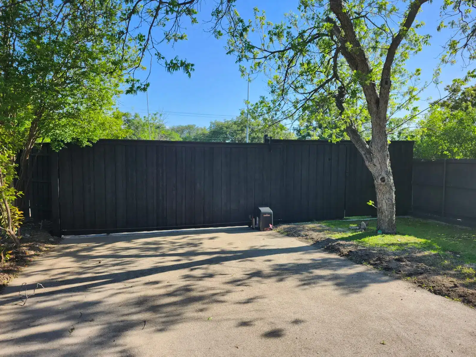 Tall dark-stained wood driveway gate with an automatic opener installed