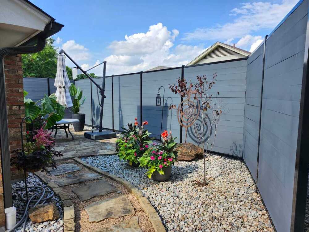 Gray horizontal-panel privacy fence with black posts around a rock garden courtyard
