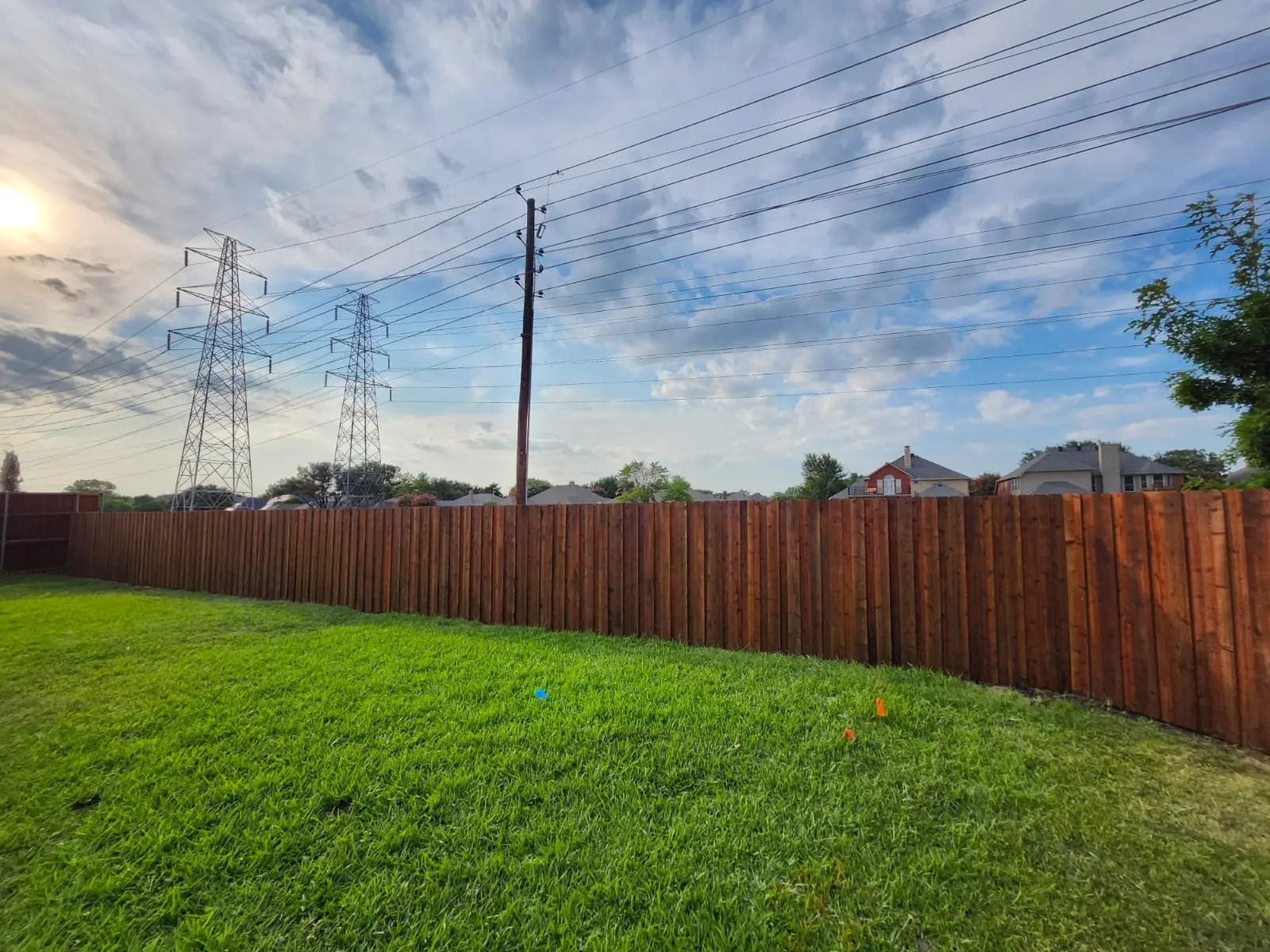 Stained cedar picket fence running the length of a green backyard lawn