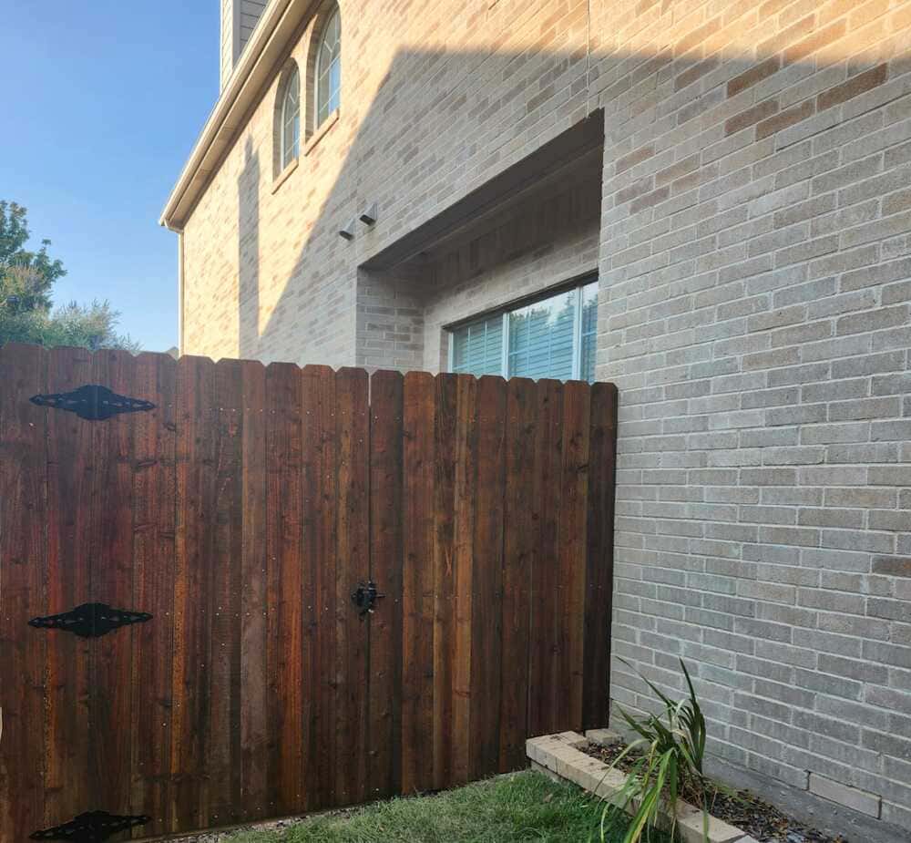 Dark-stained wood walk gate with decorative strap hinges beside a brick house