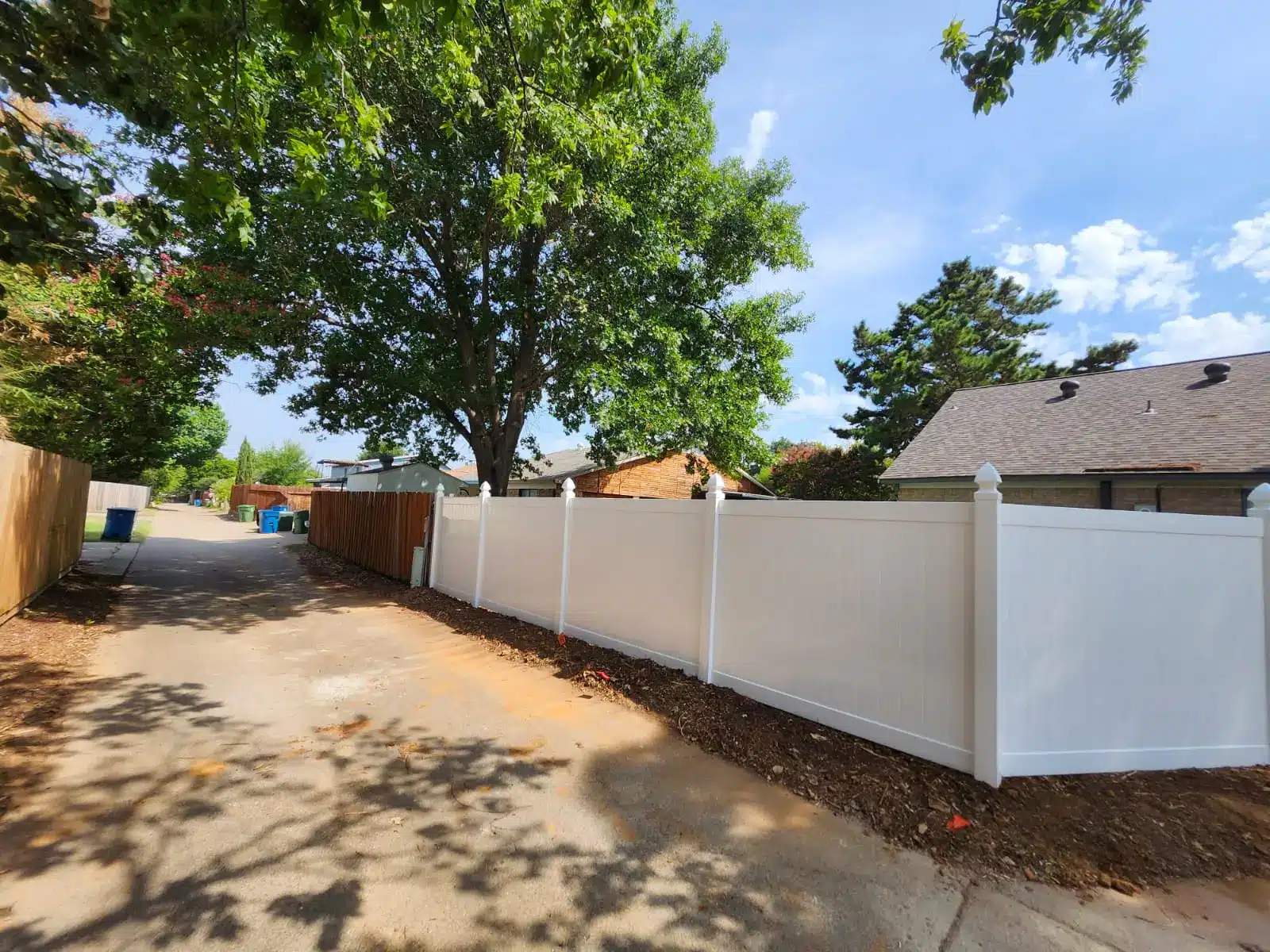 White vinyl privacy fence panels installed along an alley behind a home
