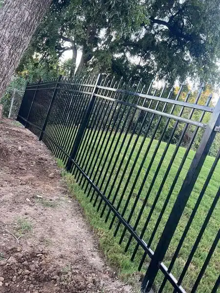 New black iron picket fence stepped along a sloped yard during installation