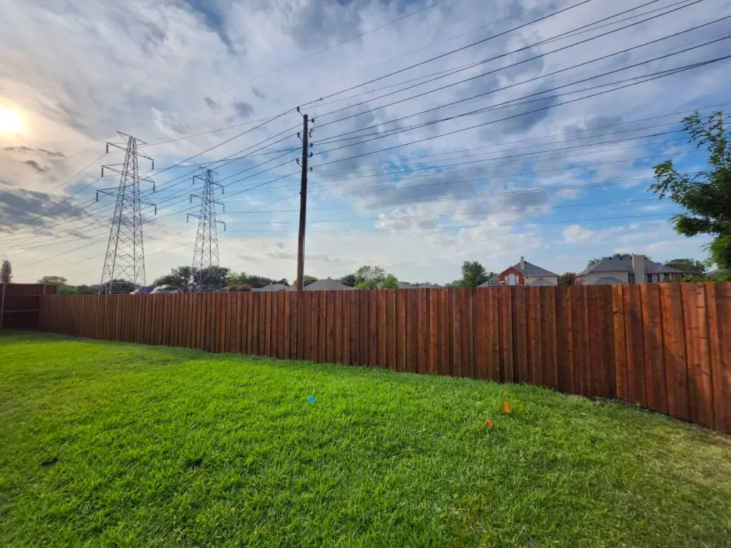 Stained board-on-board cedar fence along a green backyard lawn